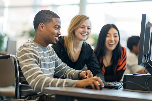Three people are sitting together, smiling, and looking at something on a computer screen.